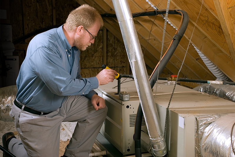 Technician kneeling to perform maintenance on a furnace.